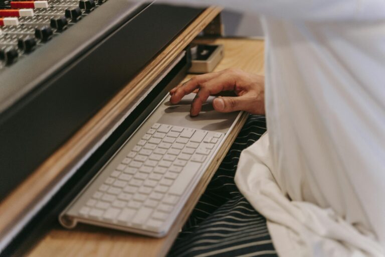 A person uses a wireless keyboard at a studio desk, illustrating modern music technology.