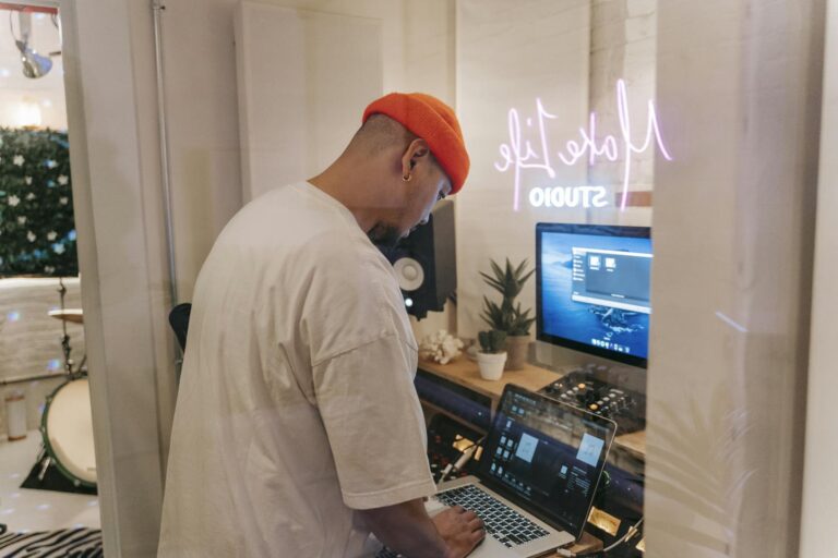 Man working on music production in a modern studio with laptop and equipment.