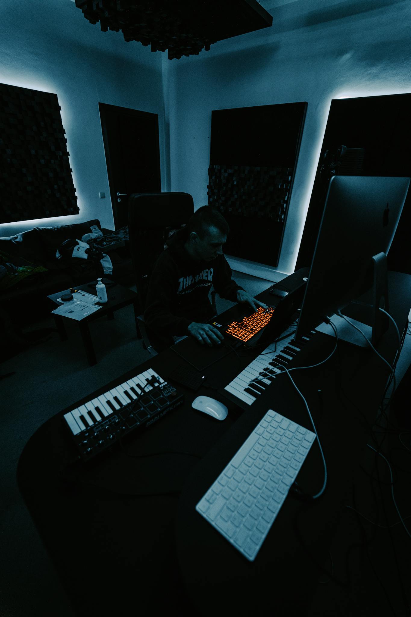 Music producer working in a dimly lit studio using a computer and keyboard equipment.